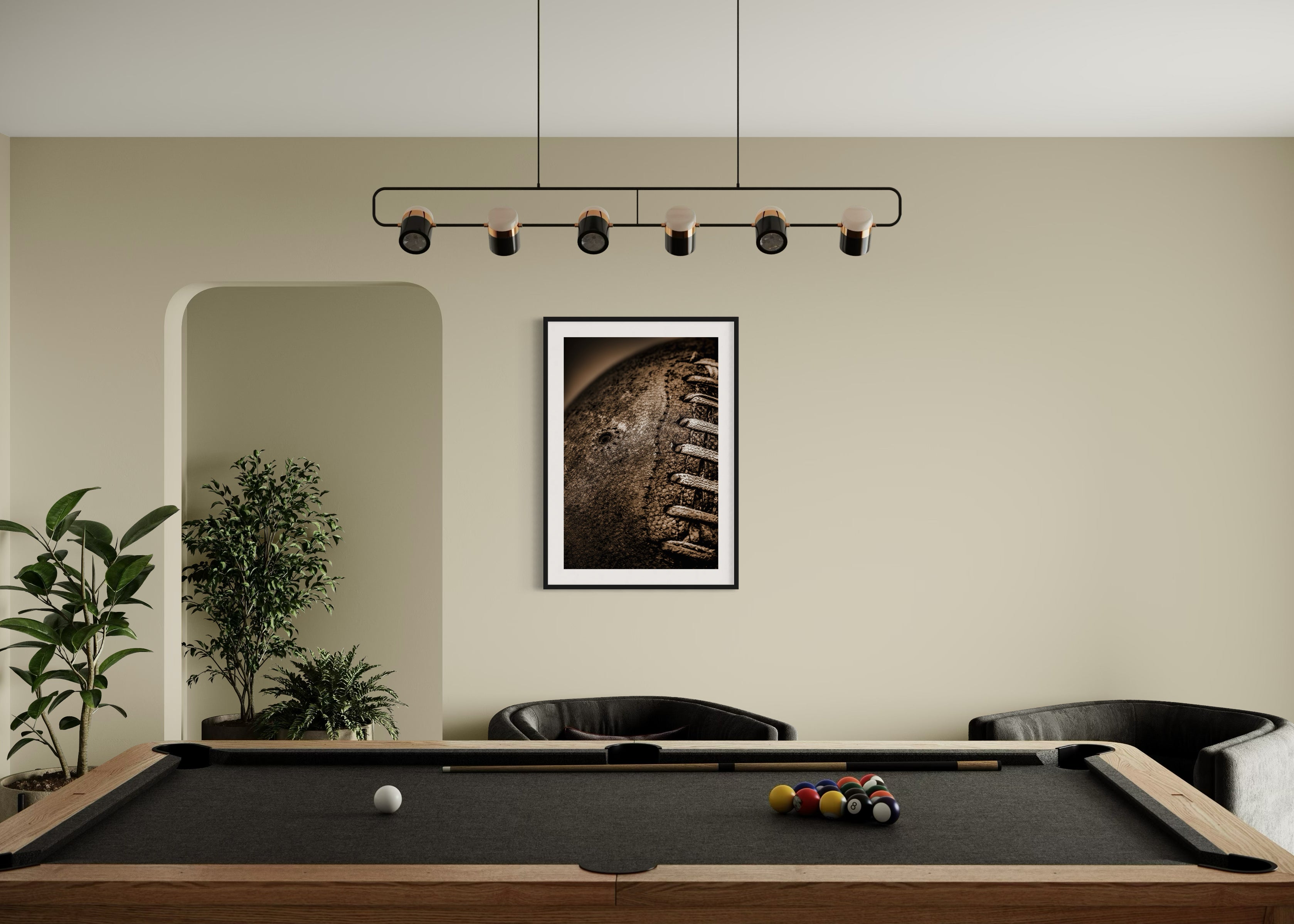 Sepia tone old football close up in a grungy look shot in studio in black frame with white matte on tan wall in game room with pool table, plants and two dark gray chairs