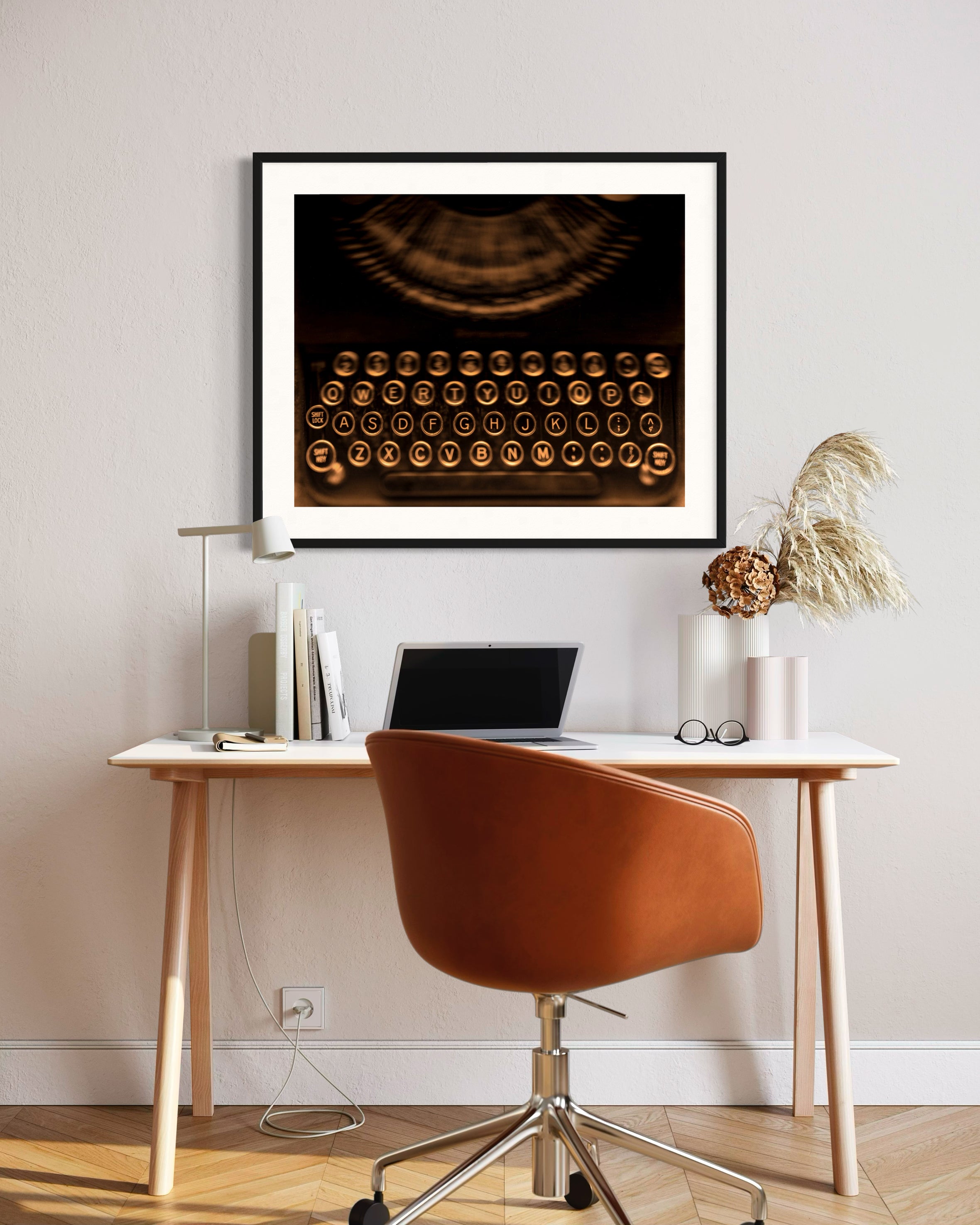 close up of old typewriter from above, horizontal black and white photo in black frame with white matte on white wall above small modern desk, orange chair, hardwood floors