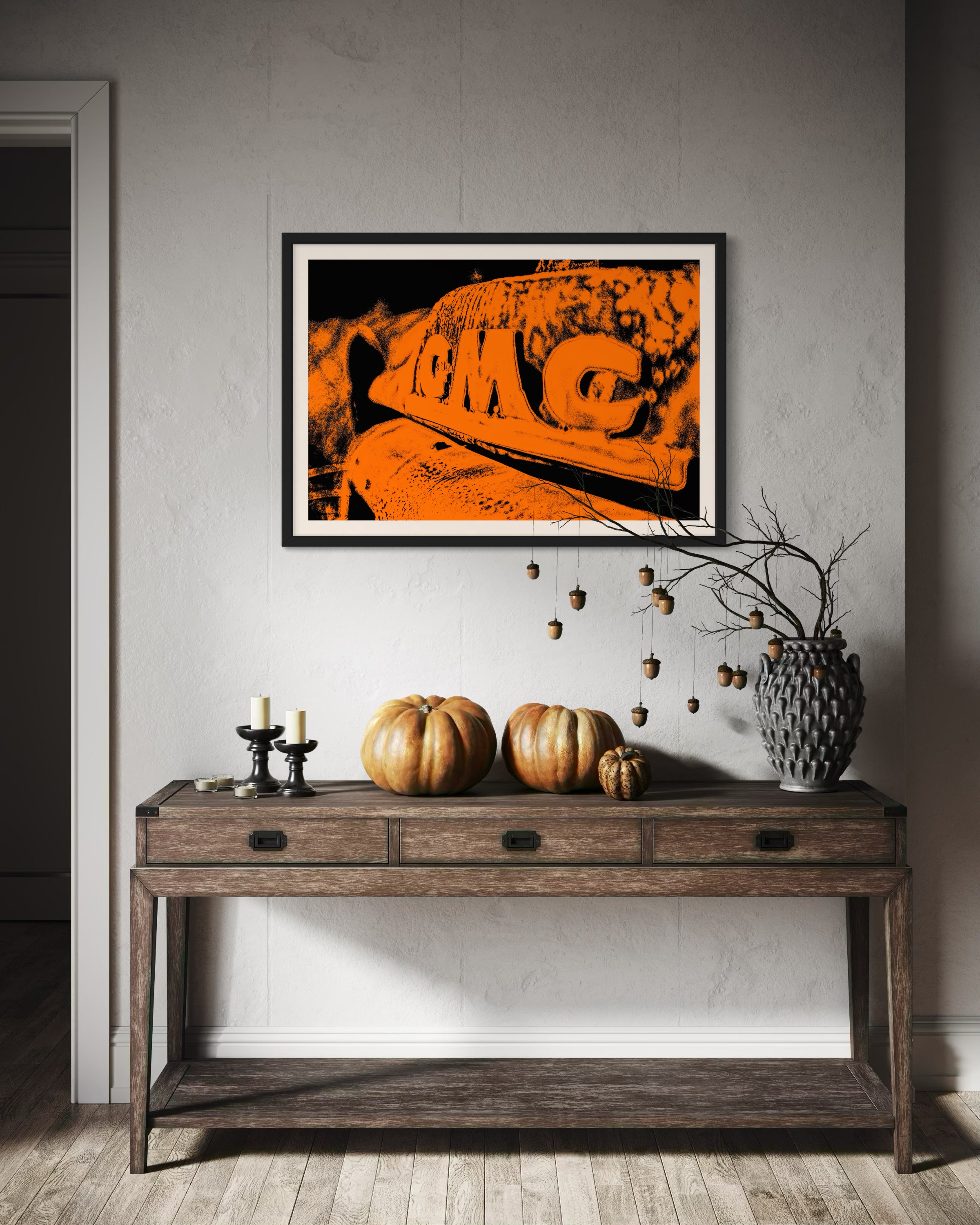 orange tone photo of front of old truck in black frame with white matte on light gray wall above wooden piece of furniture in rustic home