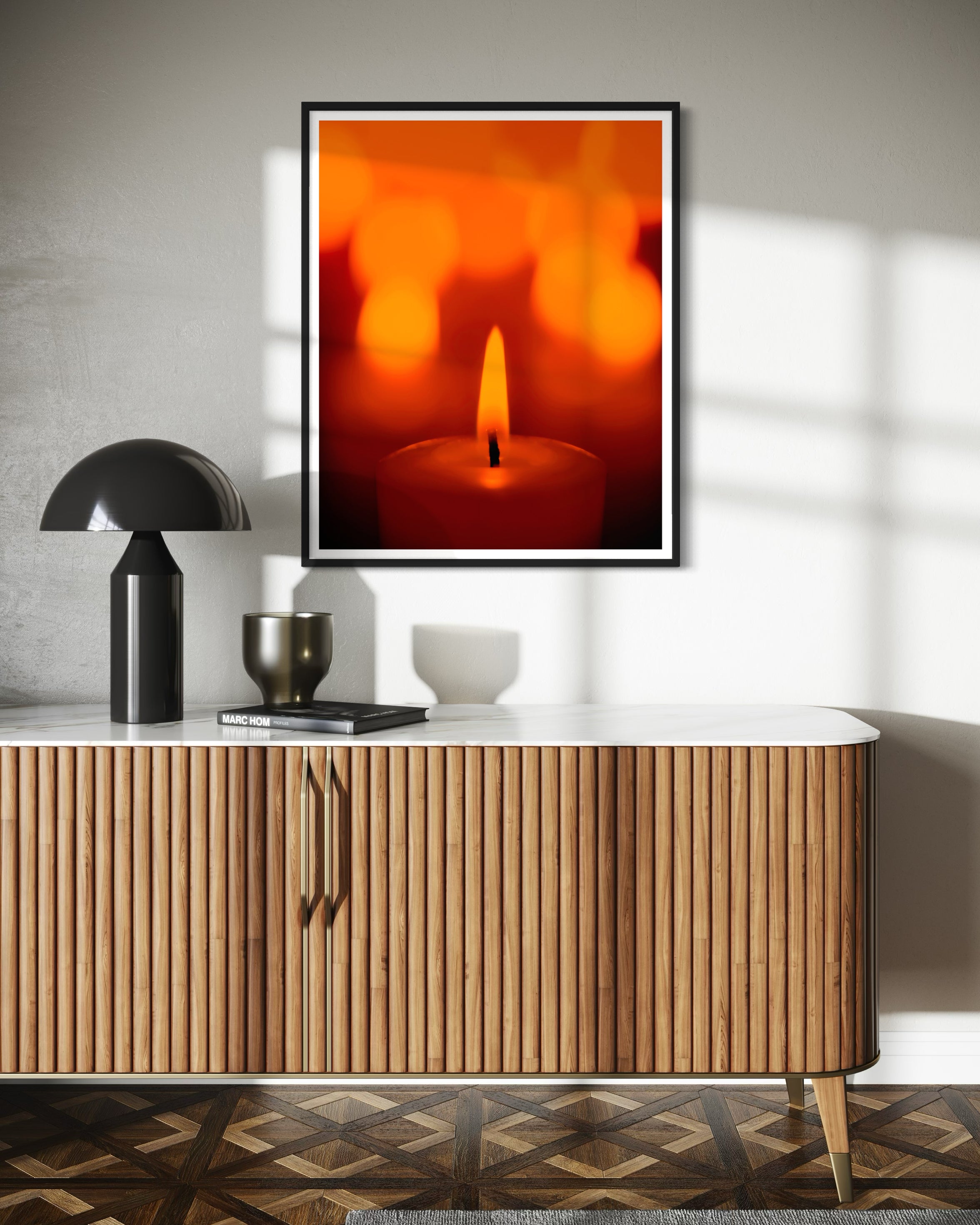 close up photo of single candle with other candles out of focus in the background in black frame with white matte on tan wall above modern furniture with white top and wooden base with sliding doors