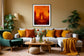 close up photo of single candle with other candles out of focus in the background in black frame with white matte on light orange wall in living room with fall colors and a few tall green plants