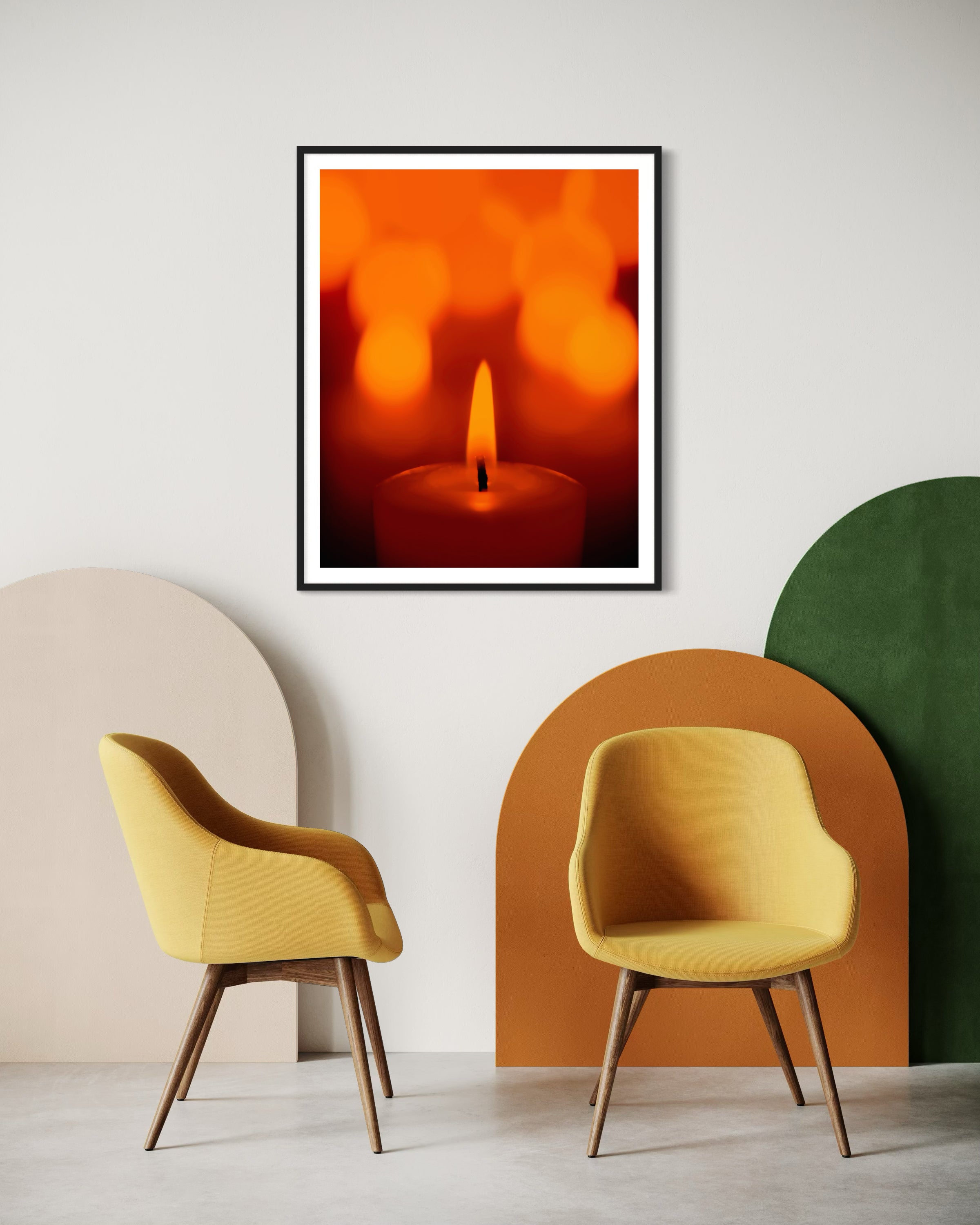 close up photo of single candle with other candles out of focus in the background in black frame with white matte on white wall in minimalist residential sitting area with sixties style furniture in orange, green and yellow 