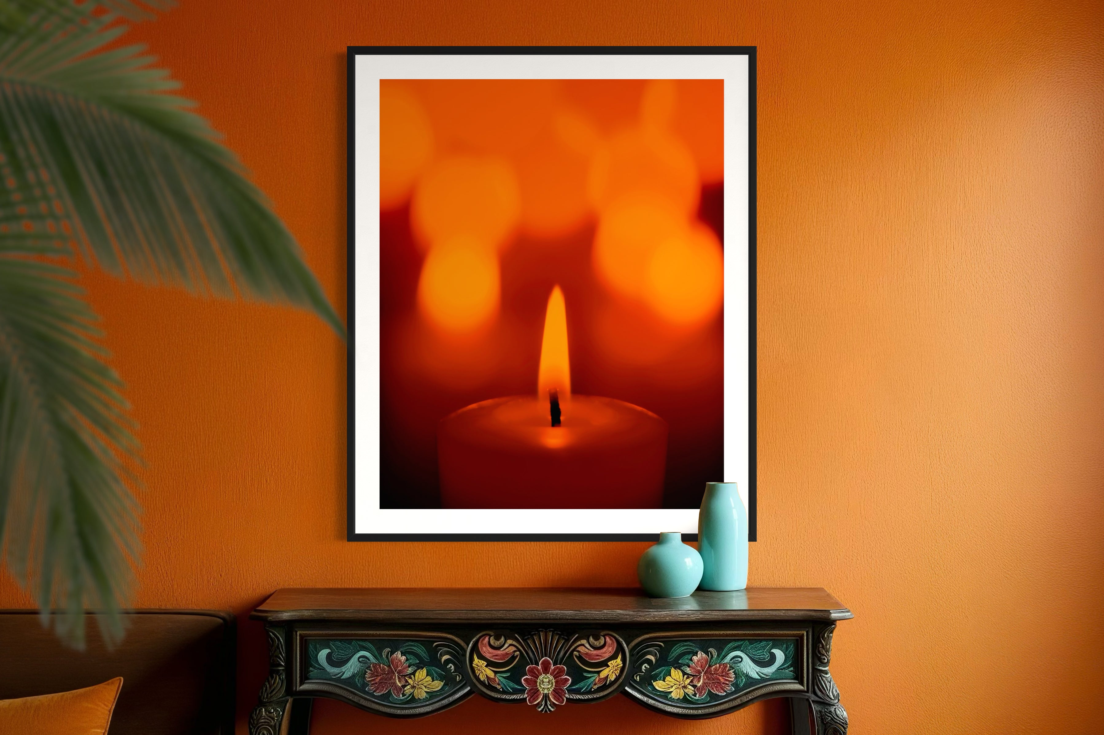 close up photo of single candle with other candles out of focus in the background in black frame with white matte on orange wall above small black table