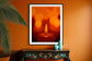 close up photo of single candle with other candles out of focus in the background in black frame with white matte on orange wall above small black table
