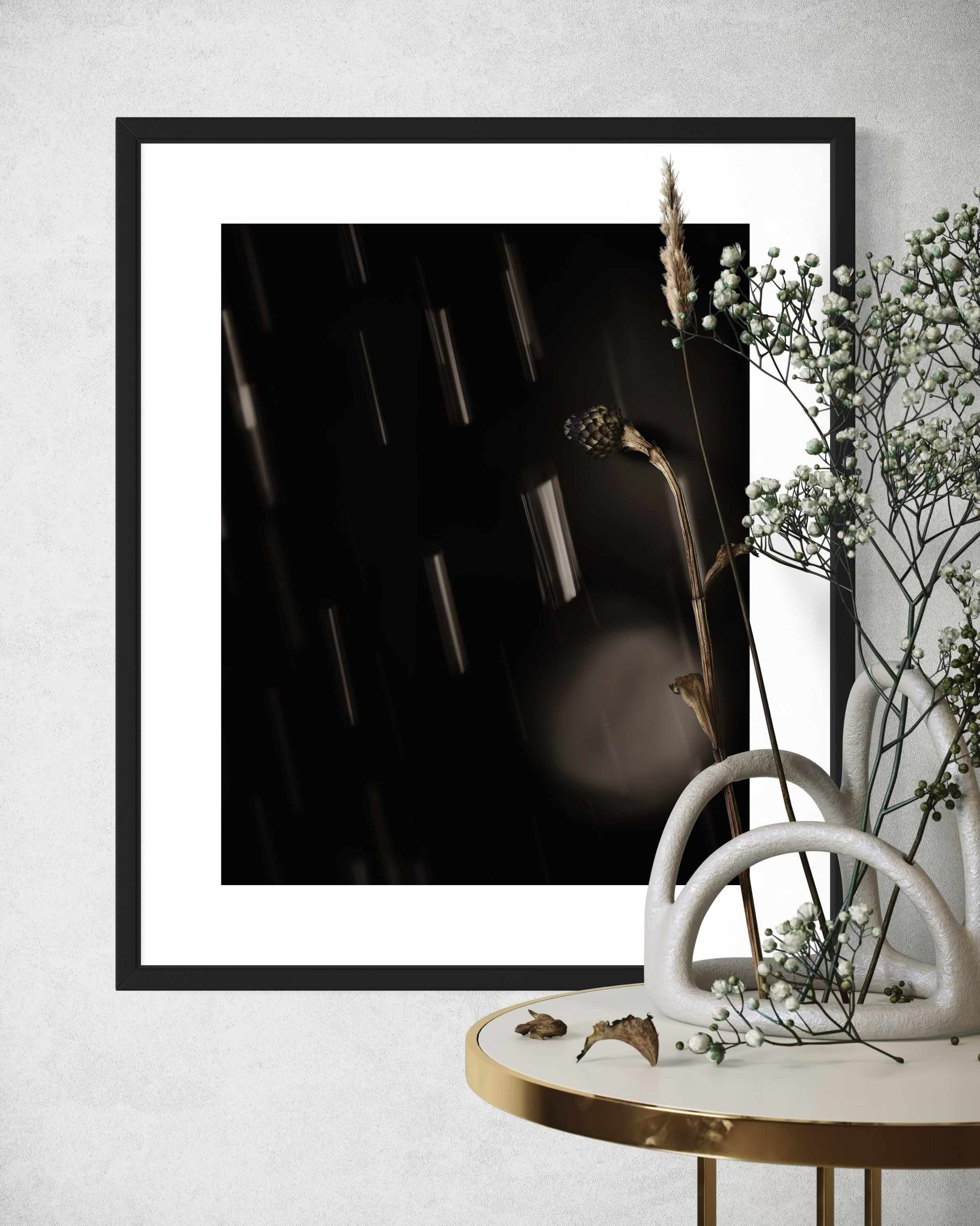 close up warm toned photo of streaks of rain in black frame on off white wall above small round table with small branches over part of the photo