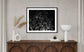 Wooden console with vases, books, and a lamp below a black-and-white abstract art piece on a beige wall. Neutral and minimalist decor.