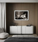 Modern living room with a white sideboard, gray sofa, and framed black and white artwork on a wooden wall.