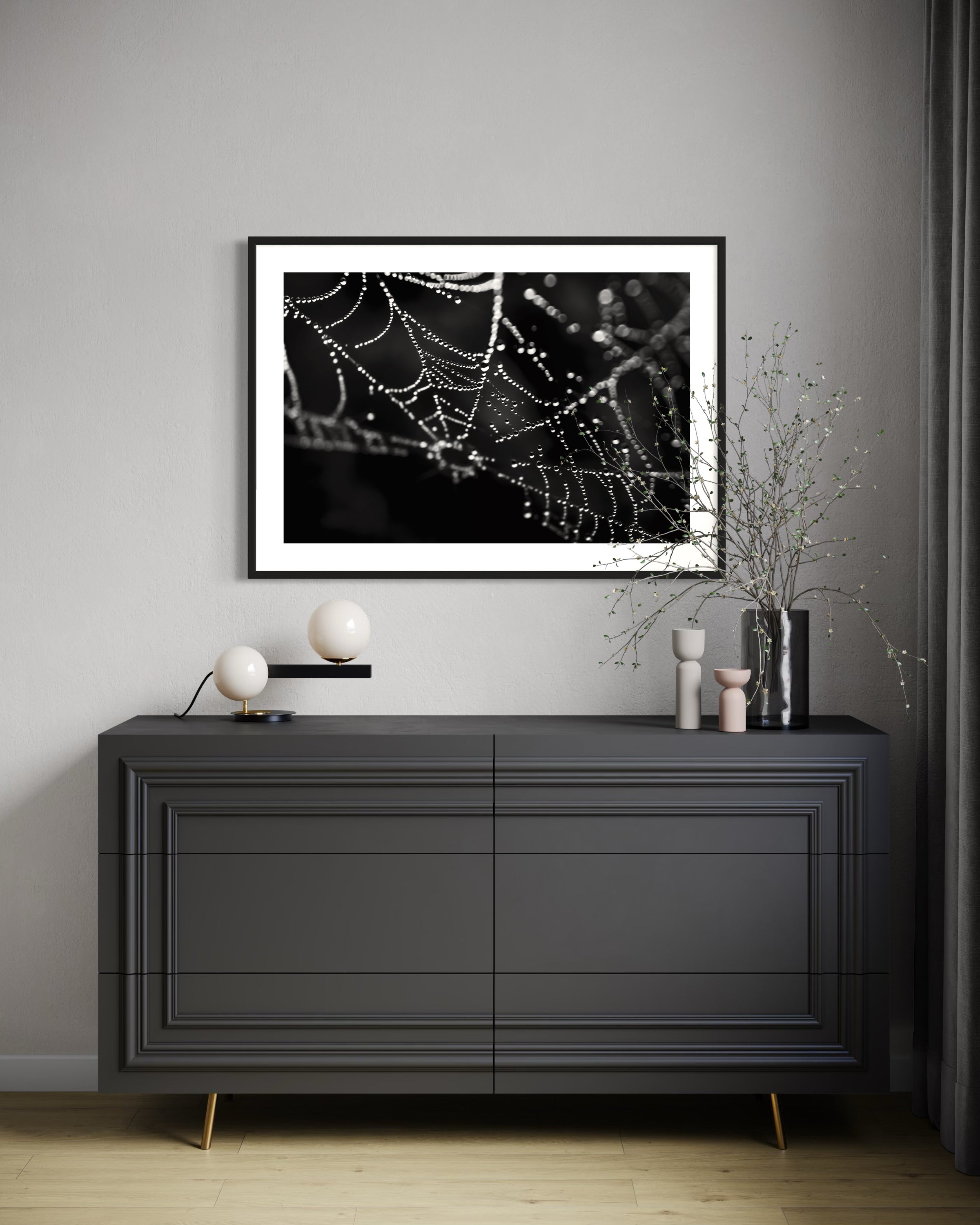 Modern interior with a black dresser against a gray wall, featuring a framed photograph of a spider web.