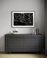 Modern interior with a black dresser against a gray wall, featuring a framed photograph of a spider web.