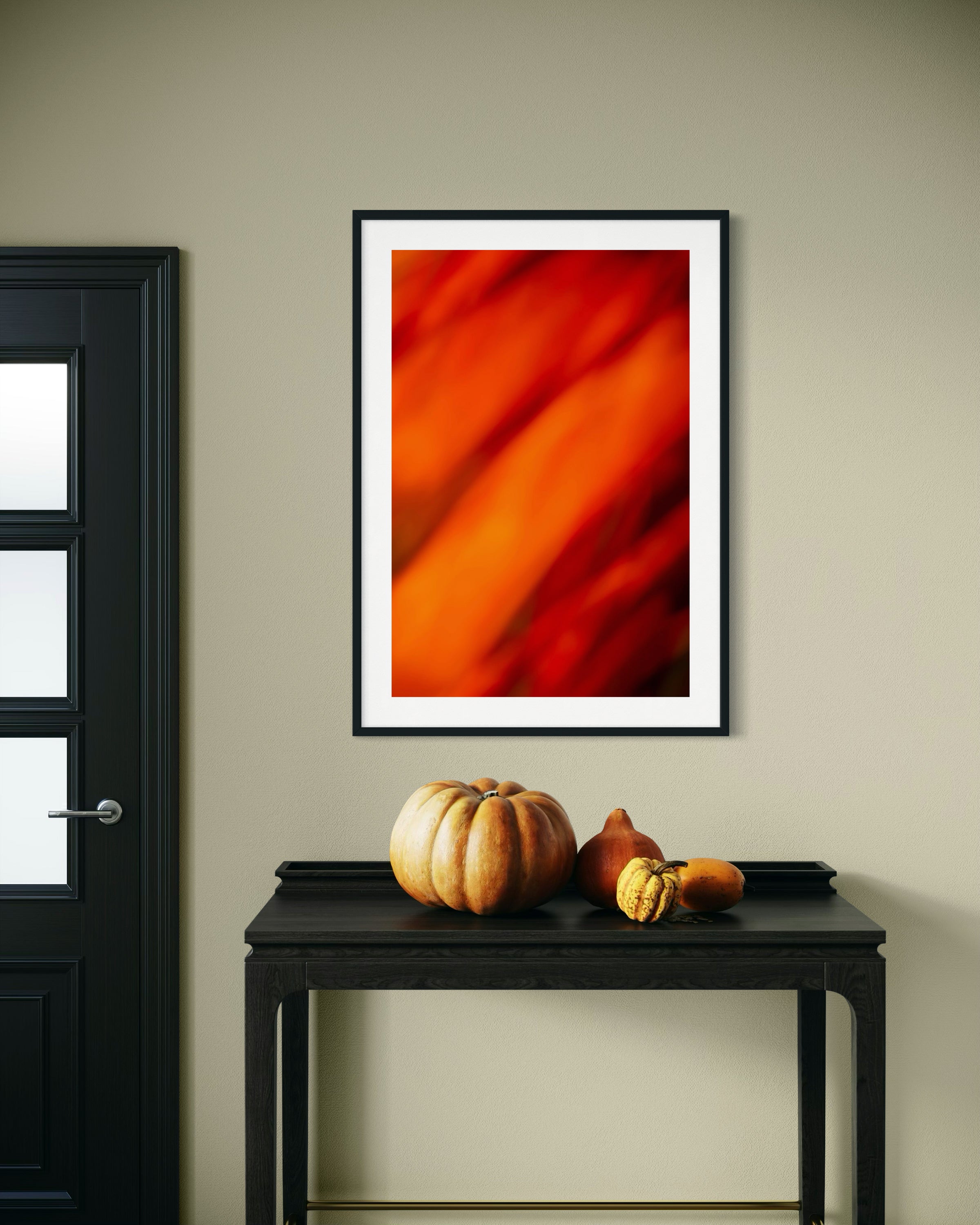 Framed abstract art on a wall above a black console table with pumpkins.
