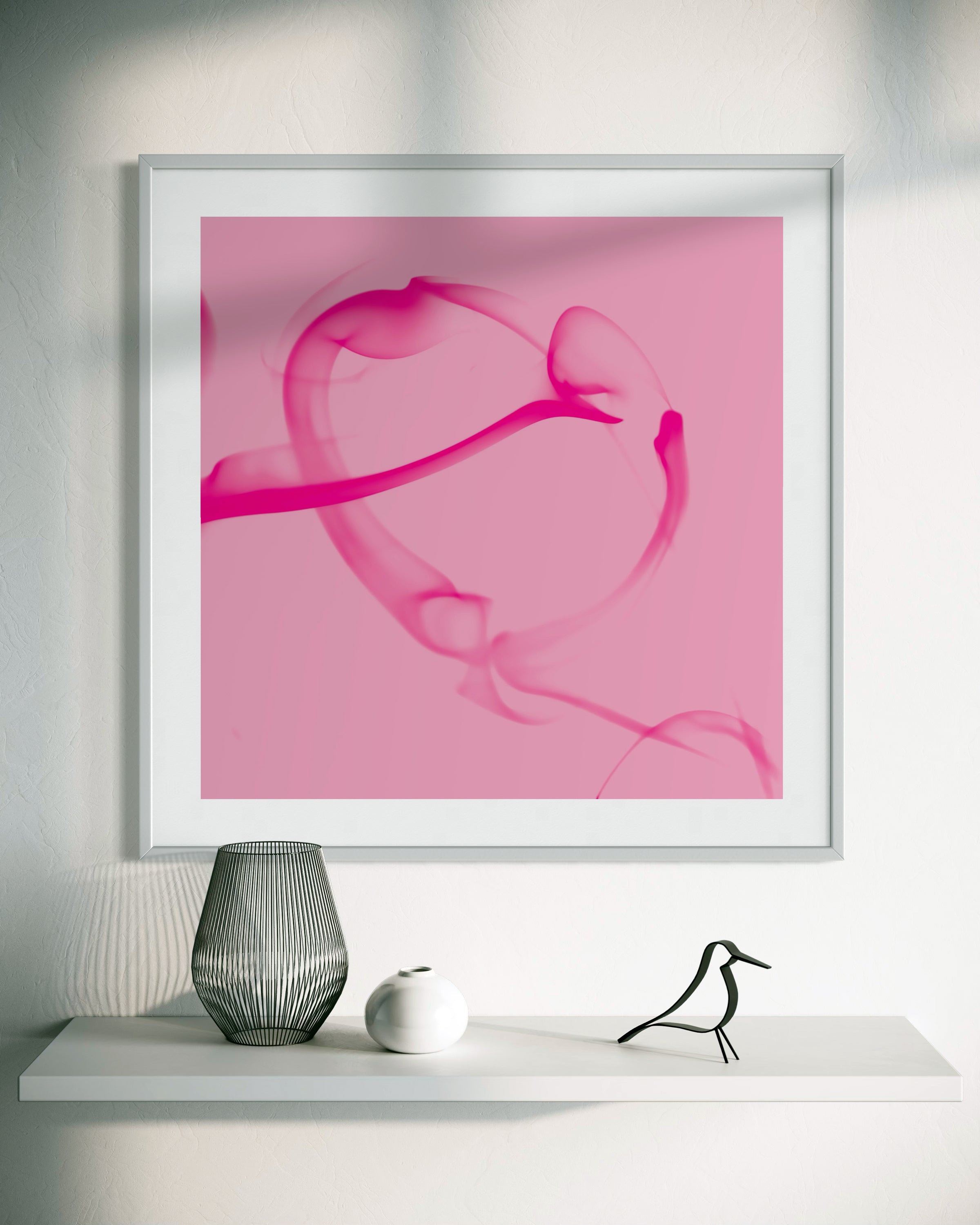 Framed abstract pink artwork on a white wall with decorative items below.