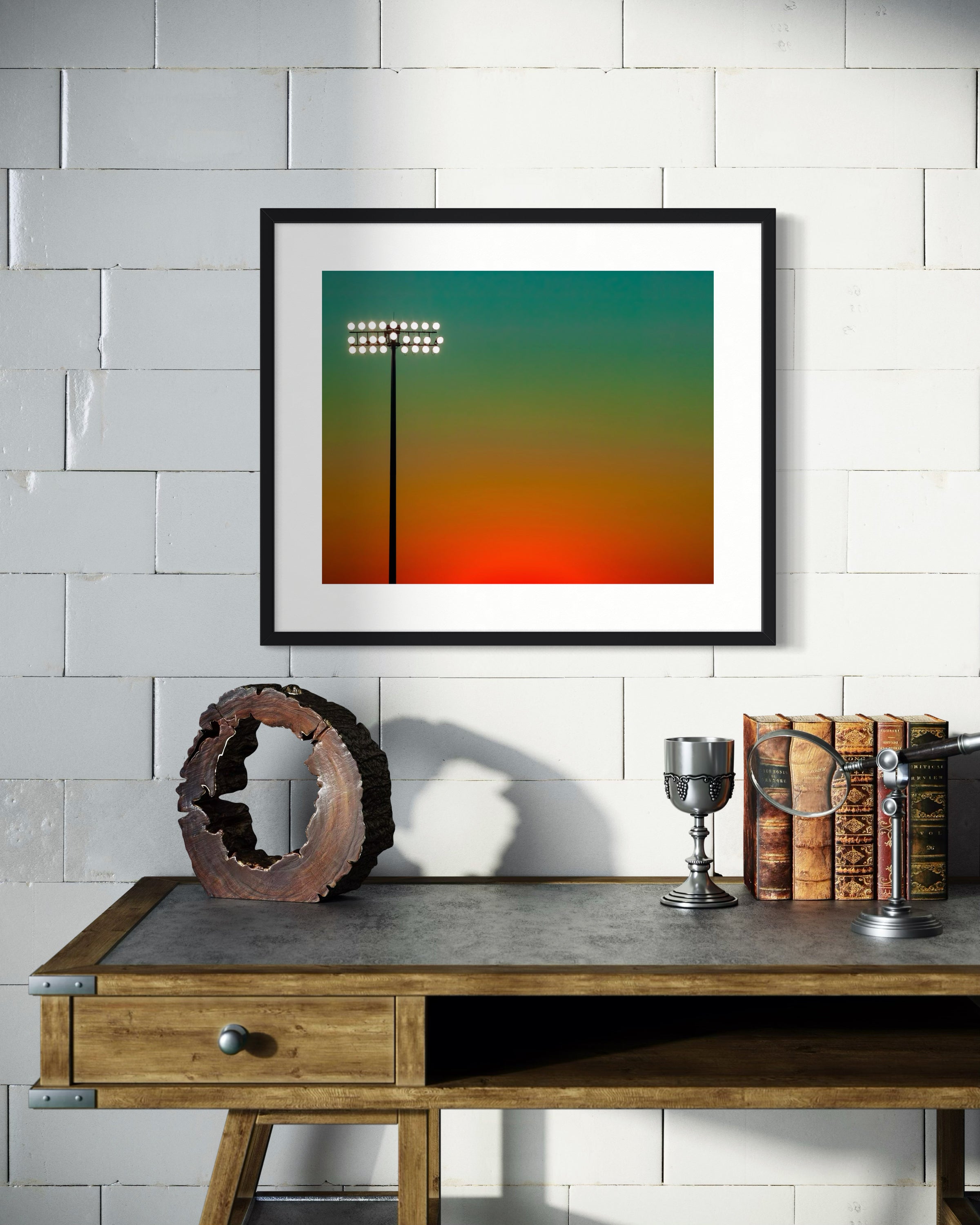 photo of stadium light at sunset in black frame on white brick wall above small small table