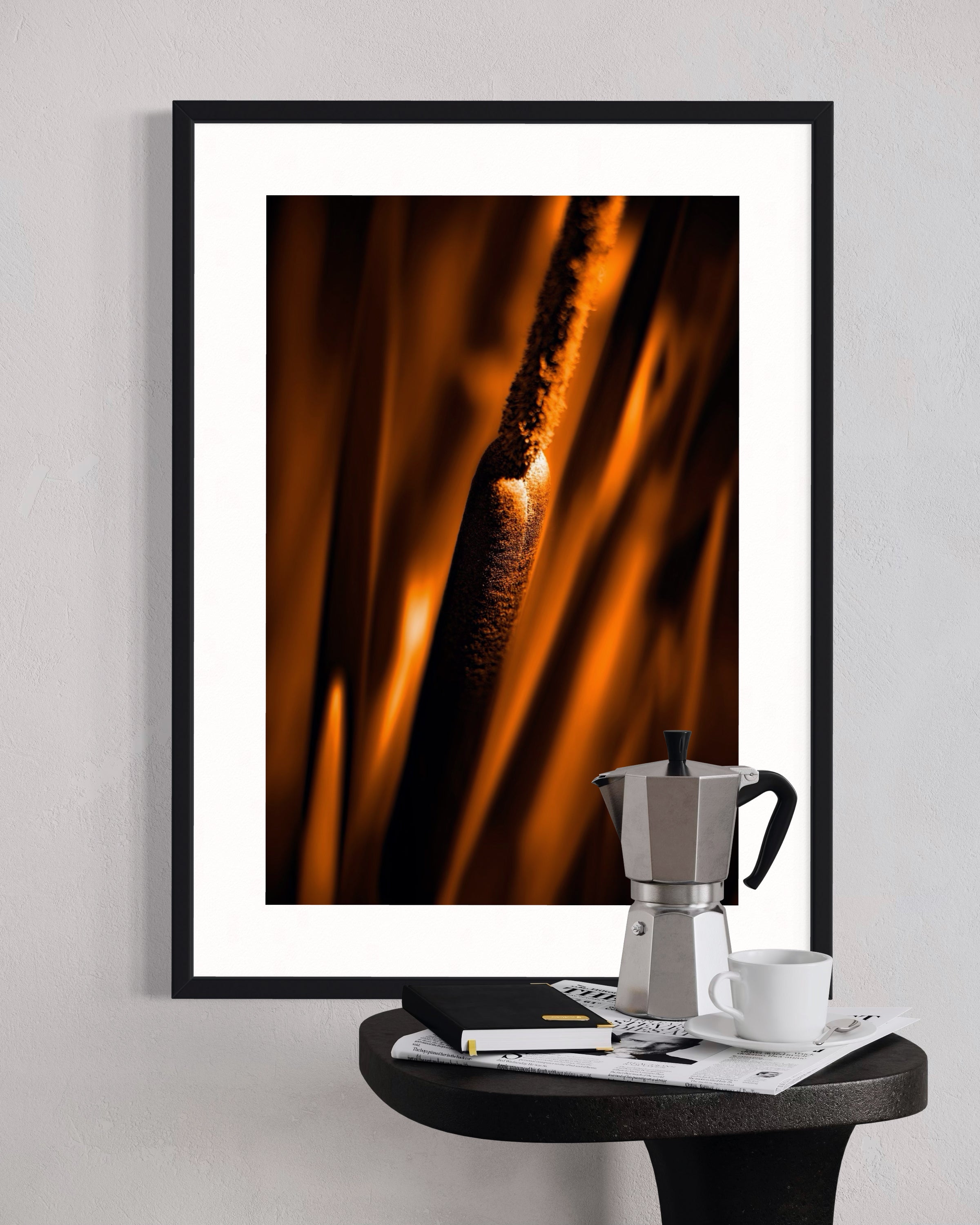 Framed abstract art print of flames on a wall above a small table with a coffee maker and cup.