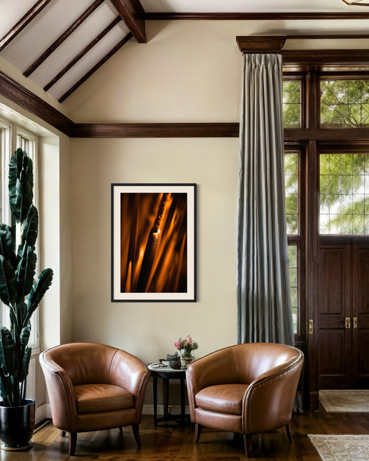 reeds in gold tone with selective focus photo in black frame on tan wall in room with hardwood floors, leather furniture and tall ceiling