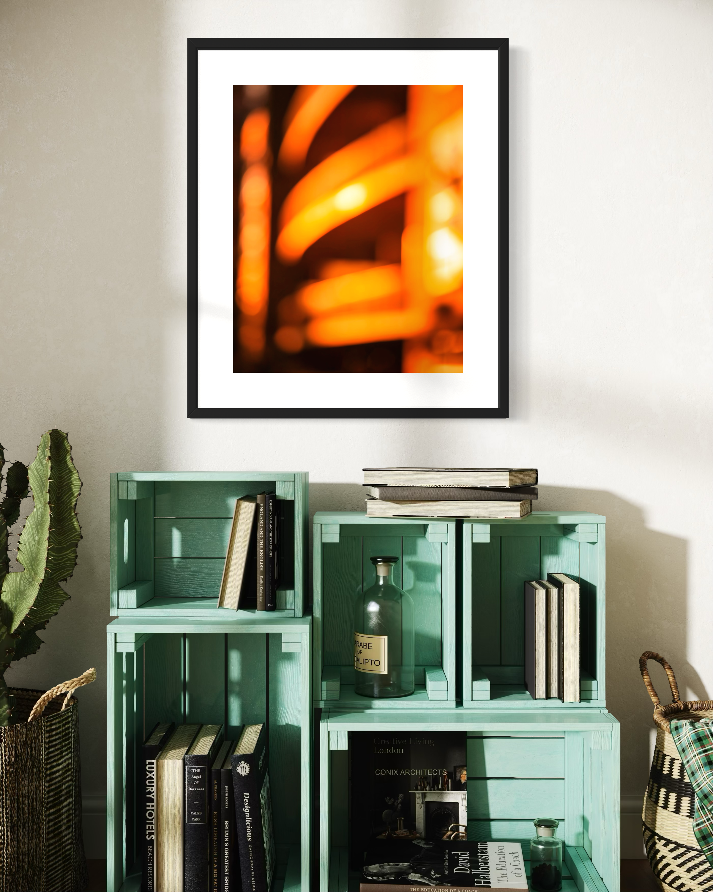 photo of abstract orange blurred lines in thick black frame with white matte on off white wall above green pastel crates used for bookshelves 