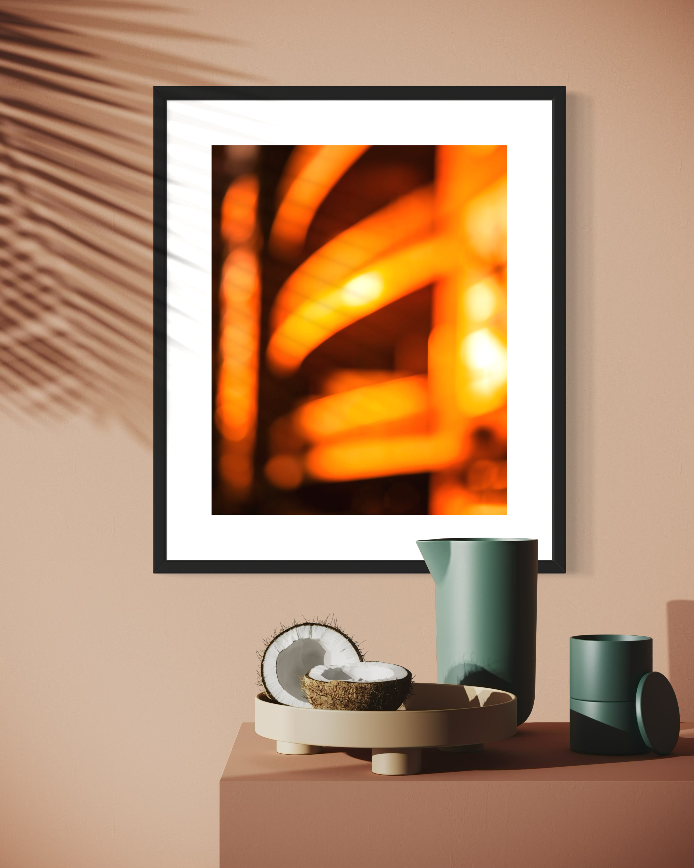 photo of abstract orange blurred lines in thick black frame with white matte pastel peach wall with shadows from palm leaf and small table, lots of earth tones