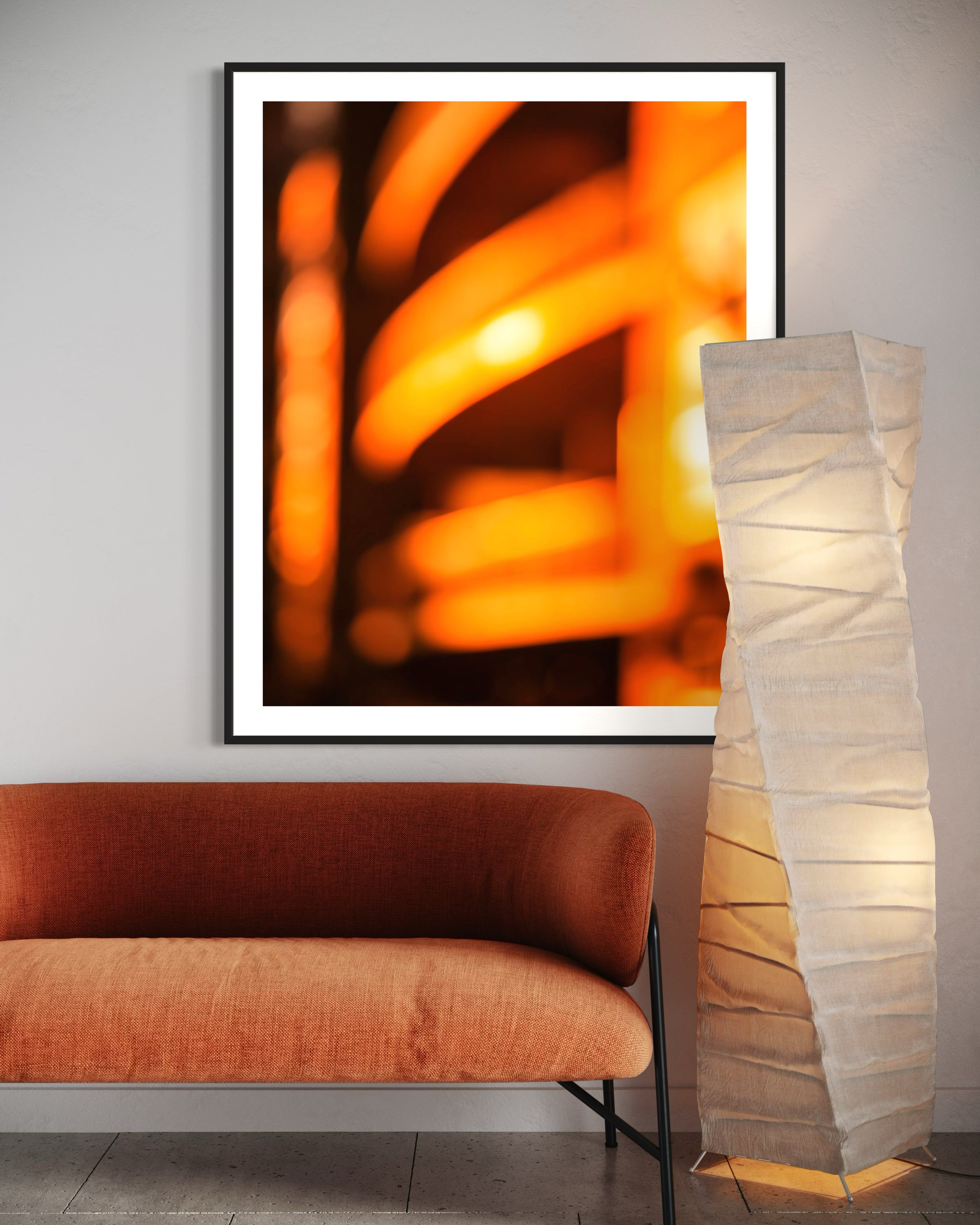 Framed abstract art piece above an orange sofa with a tall floor lamp to the right.