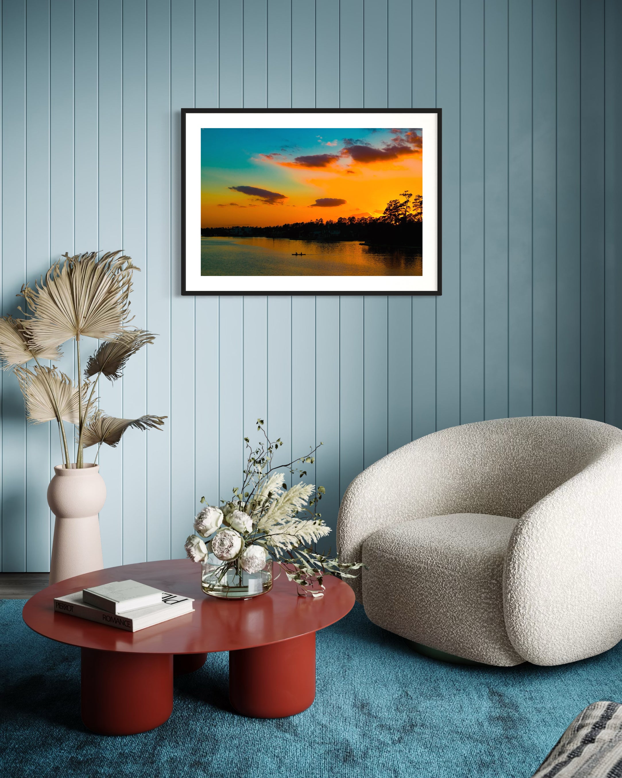 Modern living room with a framed sunset landscape, red coffee table, and beige armchair.