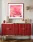 macro of pink rose shot in studio with shallow depth of field in pink frame with light pink matte on light tan wall above red piece of furniture with gold trim