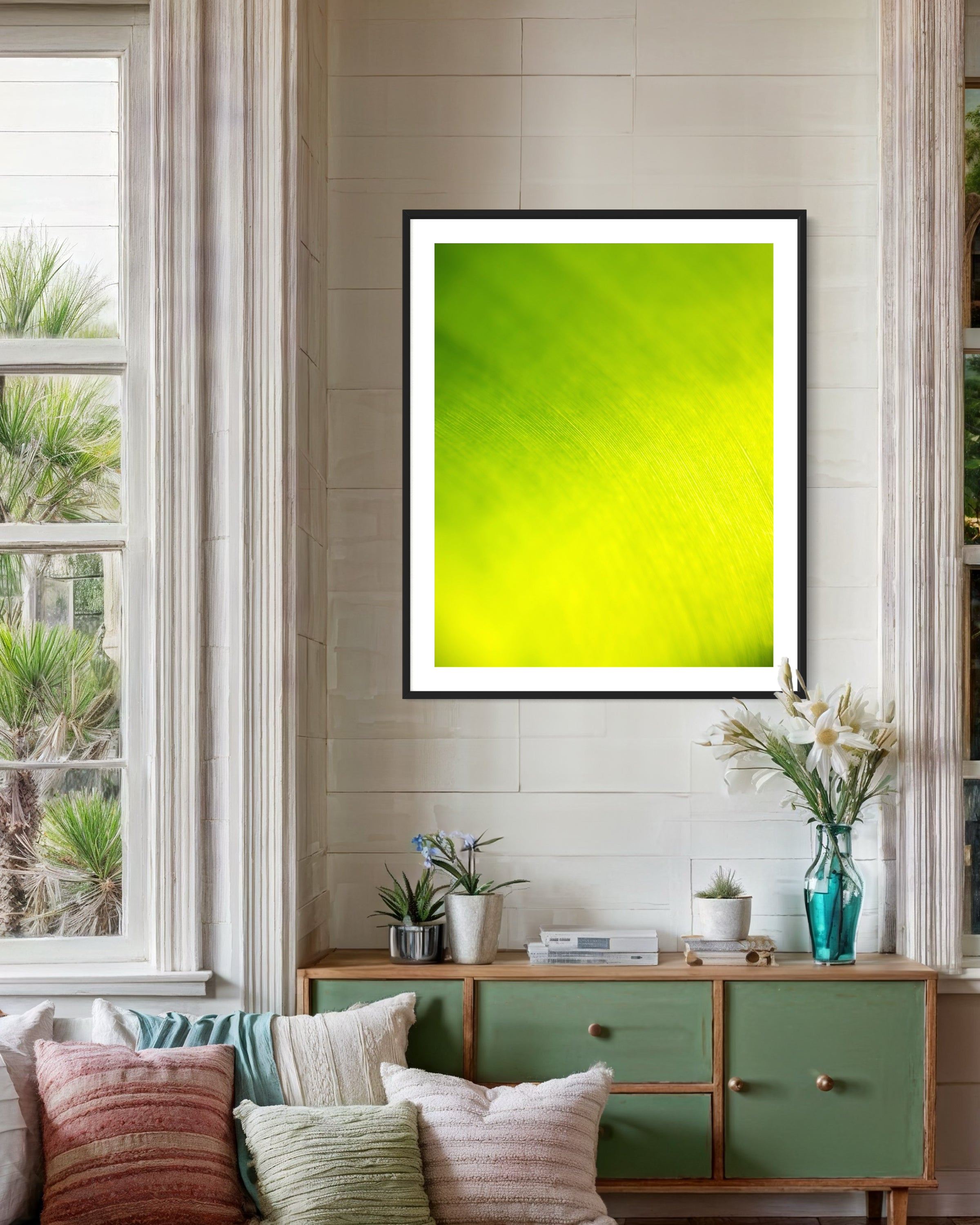 close up of large tropical leaf with the lines flowing like a waterfall in black frame with off white matte on white wall wall above small green piece of furniture in cozy sitting area