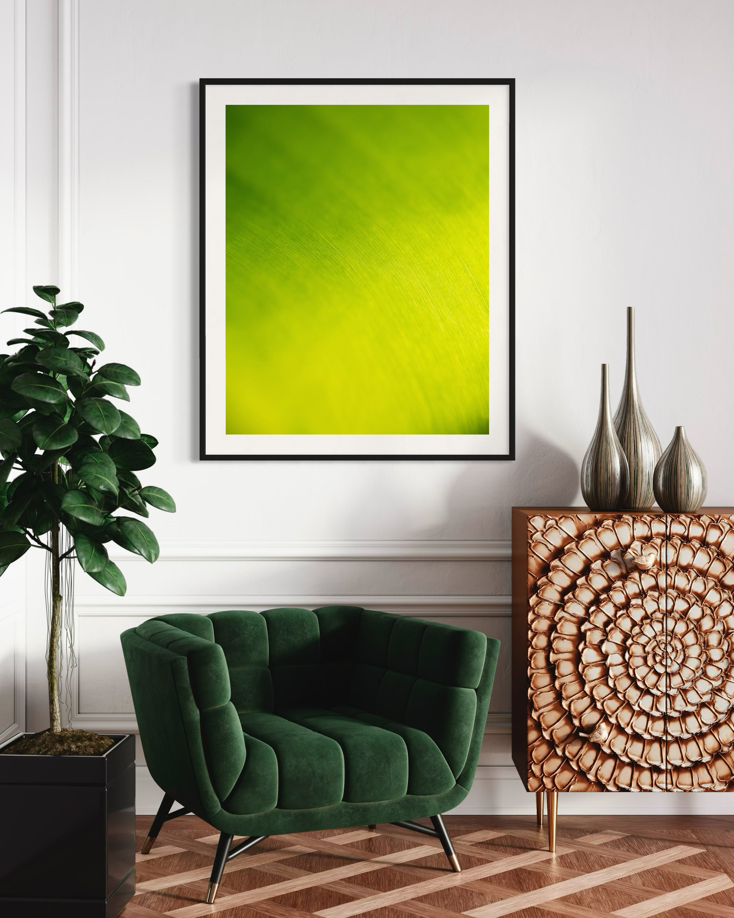 close up of large tropical leaf with the lines flowing like a waterfall in black frame with off white matte on white wall wall in sitting area with green chair and tall green plant