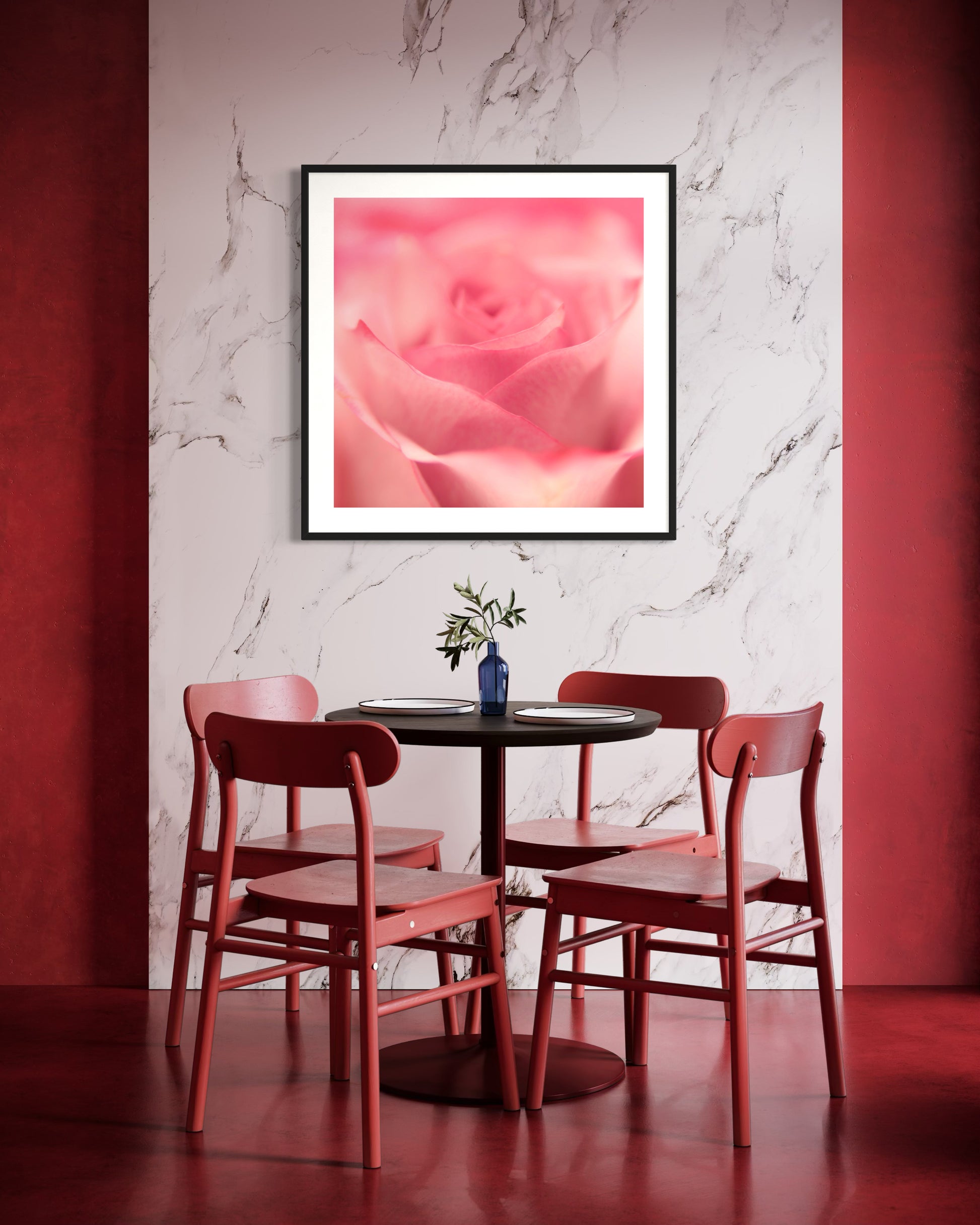 macro of pink rose shot in studio with shallow depth of field in black frame with white matte on white marble wall above small round table with 4 pinkish red chairs