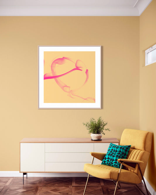 abstract pink heart on tan background in tan frame with white matte on pastel yellow wall in minimalist sitting area with golden yellow chair