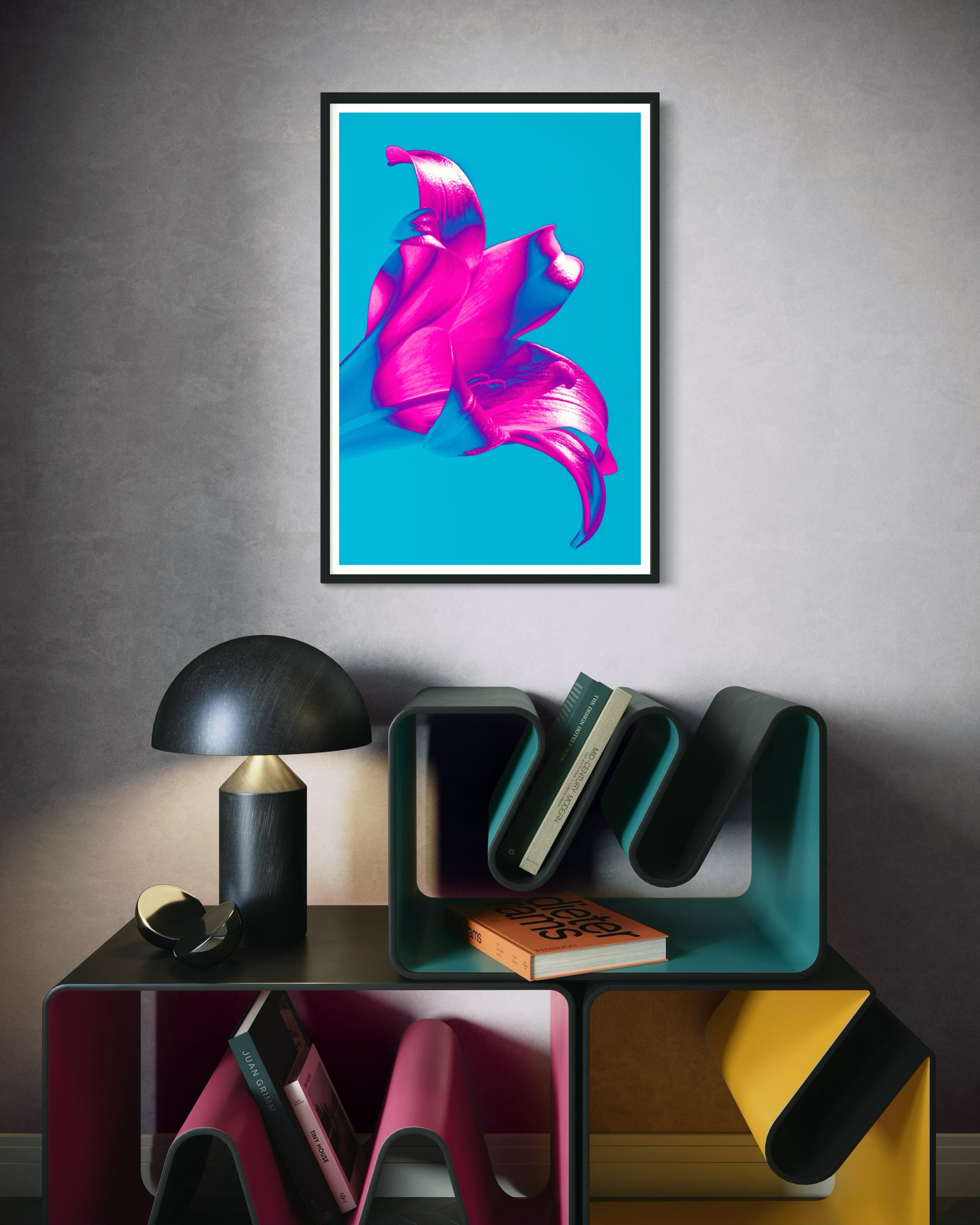bright pop art photo of pink lily on blue background in black frame with white matte on light gray wall above small funky multicolored stacked shelves with small lamp