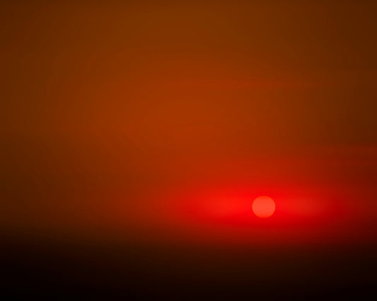 photo of hazy orange sunset, a few horizontal clouds, sun in lower right of the frame