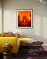 close up photo of single candle with other candles out of focus in the background in black frame with white matte on light tan wall in modern living room with bright yellow couch