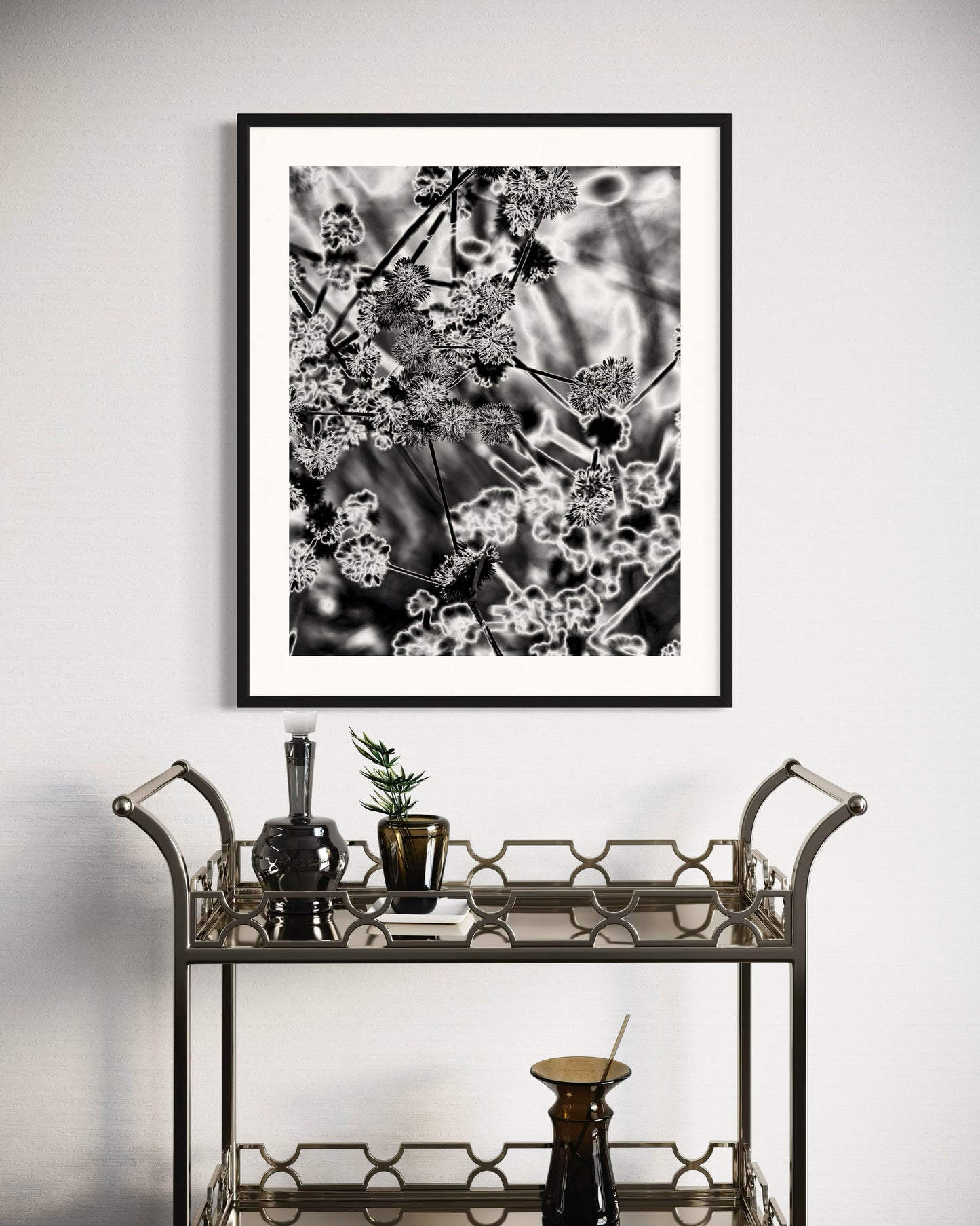 black and white close up of plant with solarized effect in black frame with white matte above modern small steel serving table with glassware 