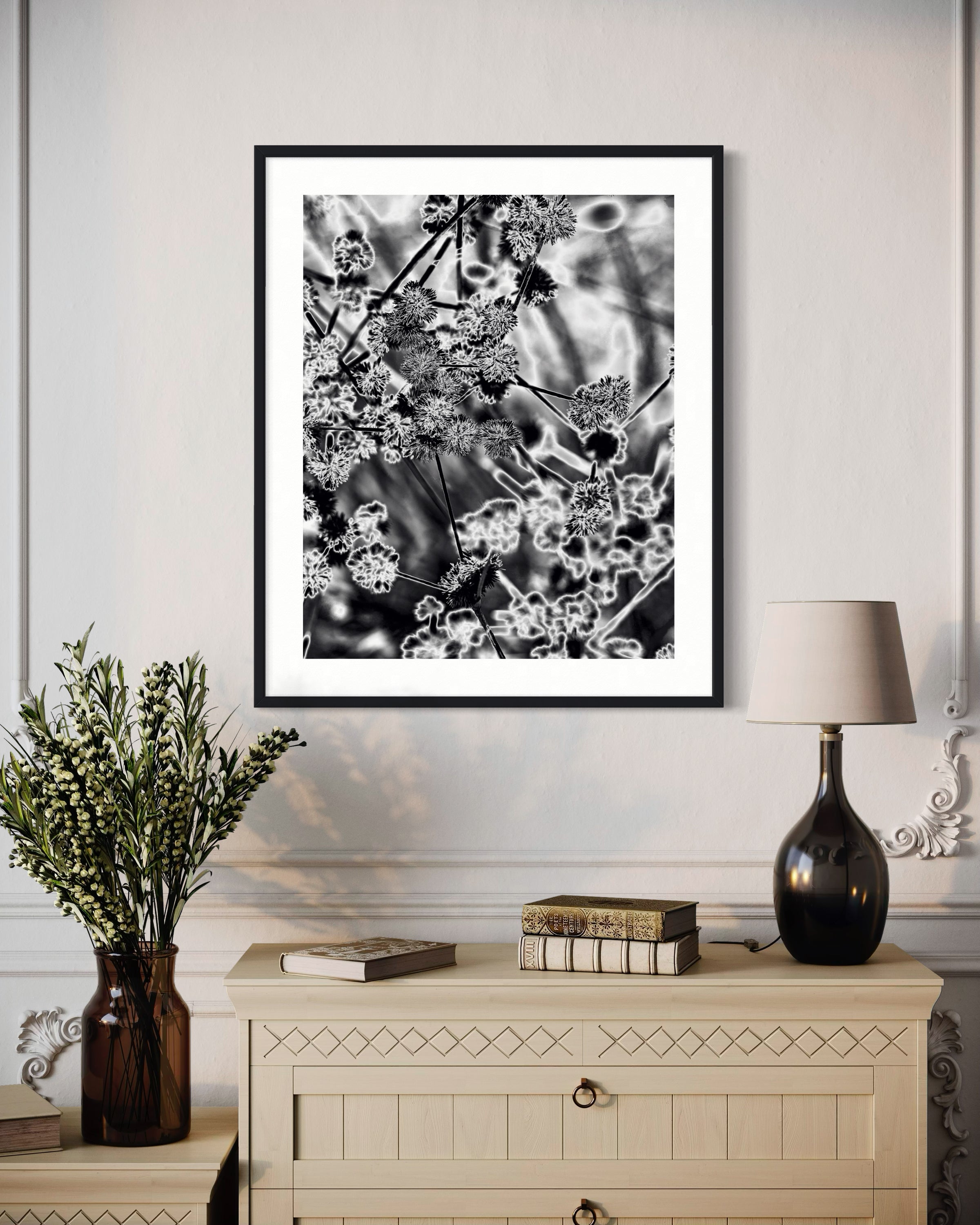 Framed black and white artwork on a wall above a wooden cabinet with decorative items.