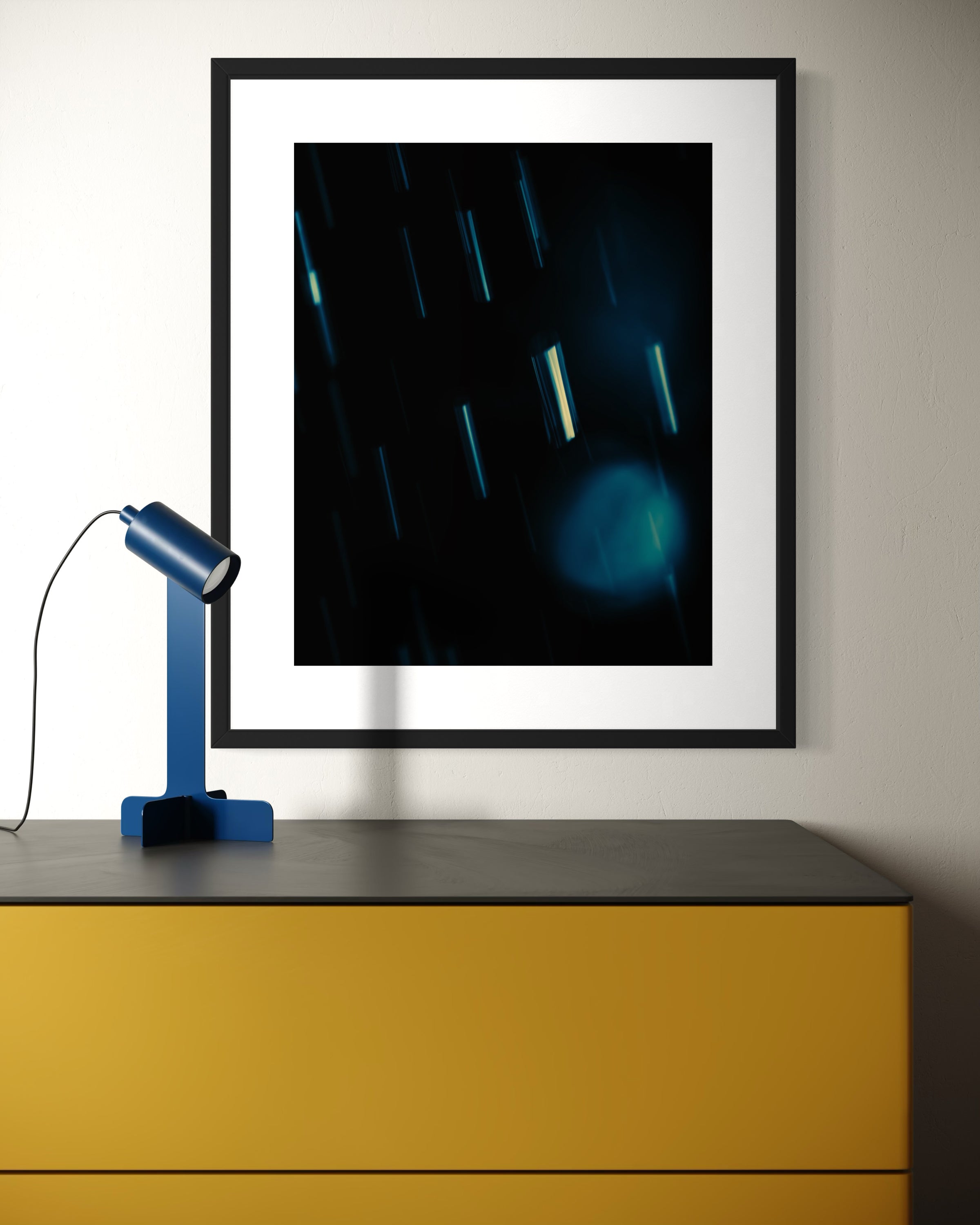 close up cool toned photo of streaks of rain in black frame with white matte on white wall above modern yellow table with black top